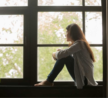 stock image of a woman sitting in the window sill of large windows