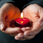photo of someone holding a burning, red, heart-shaped candle in their hands