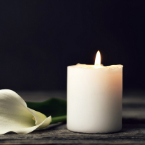 photo of a burning white candle sitting on a table next to a white flower