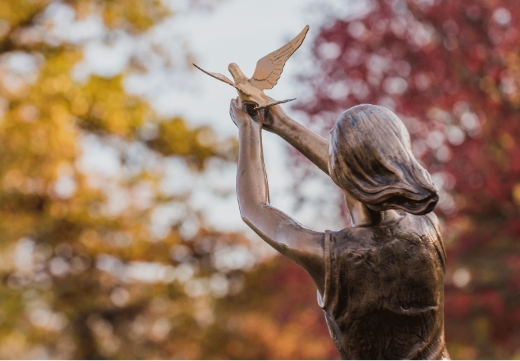 photo of a bronze sculpture of a girl releasing a dove