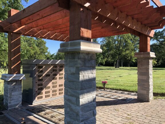 Photo of a brick pergola with a red wood stained roof and memorial plaques within the ground and wall