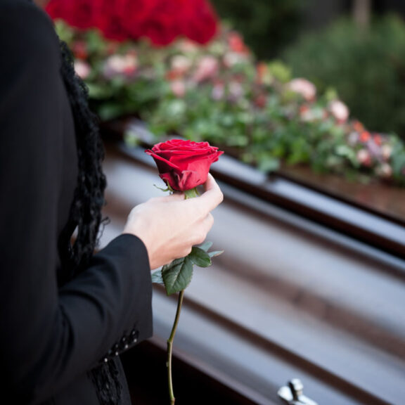 photo of someone dressed in black holding a red rose with a casket in the background
