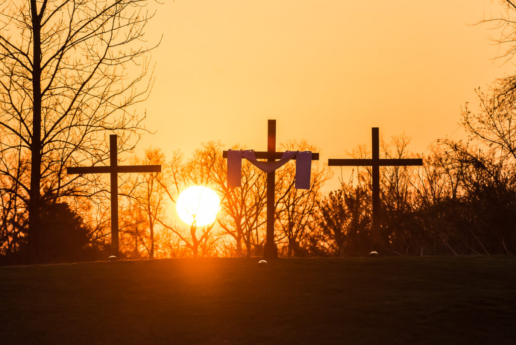 Image of three wooden crosses at the top of a hill with the sunrise behind them